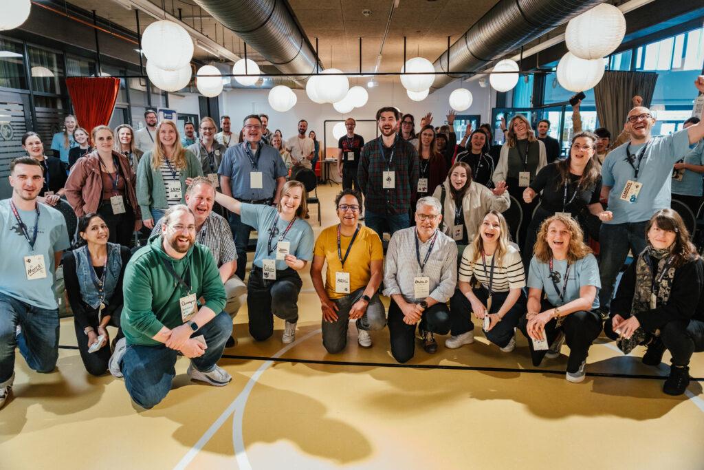 Gruppenbild mit allen Teilnehmer:innen im Hintergrund sowie dem Orga-Team und den Session Hosts im Vordergrund.